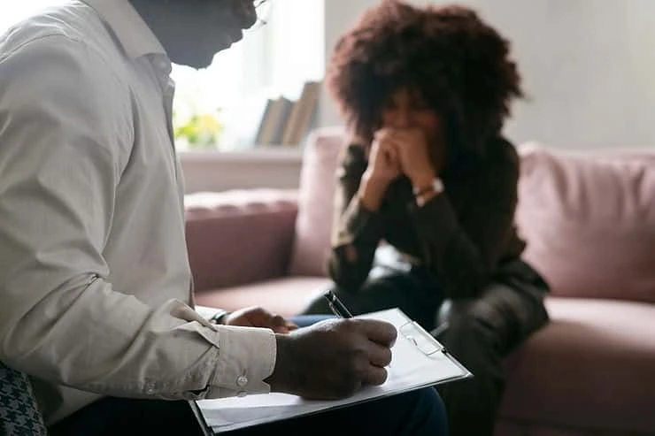 Mental health provider taking notes during a PTSD treatment consultation with a patient seated on a couch