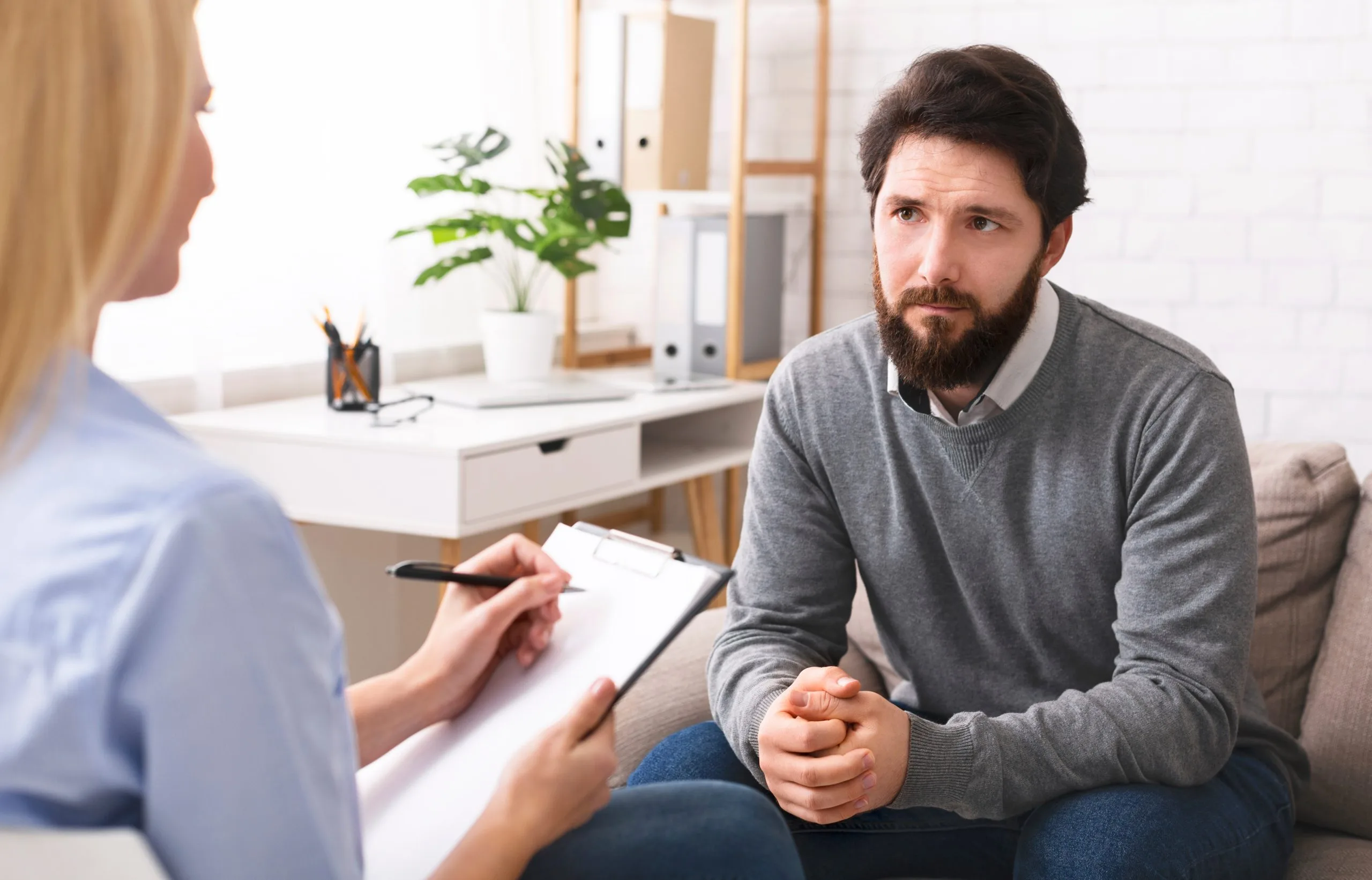 Stressed man in therapy session with a clinician taking notes at a desk