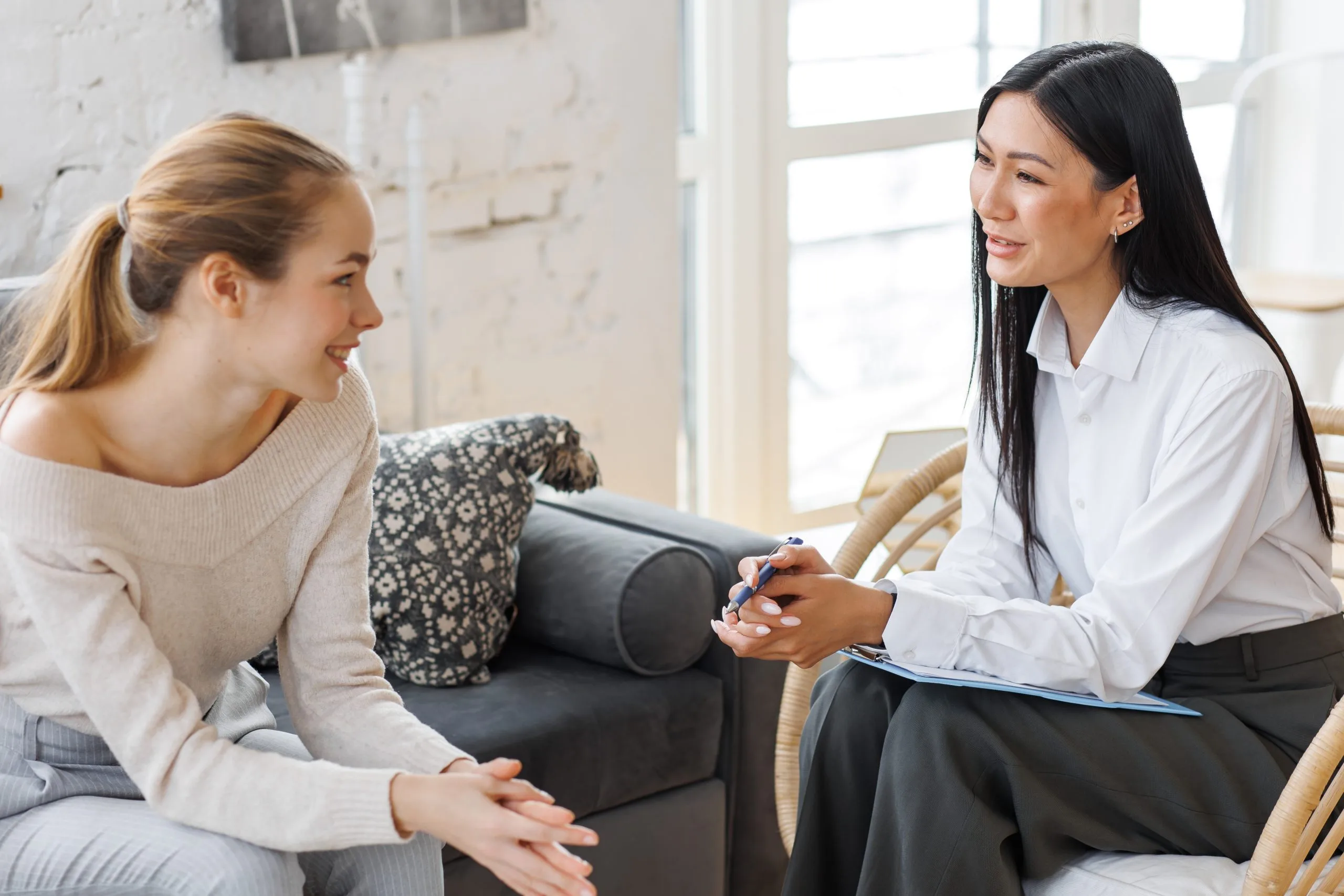 Healthcare provider in white coat taking notes during a consultation with a patient in a bright office setting