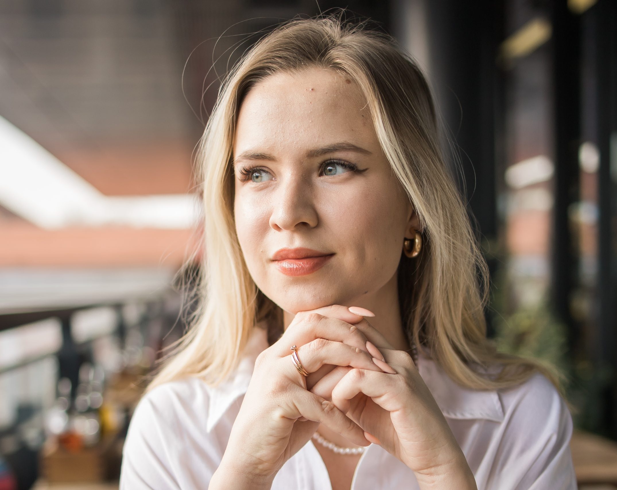 Young woman with blonde hair smiling thoughtfully on a café balcony