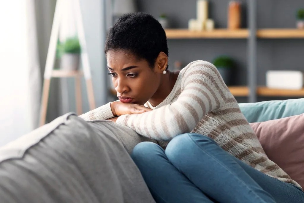 Woman sitting on a couch with a contemplative expression, hand to face