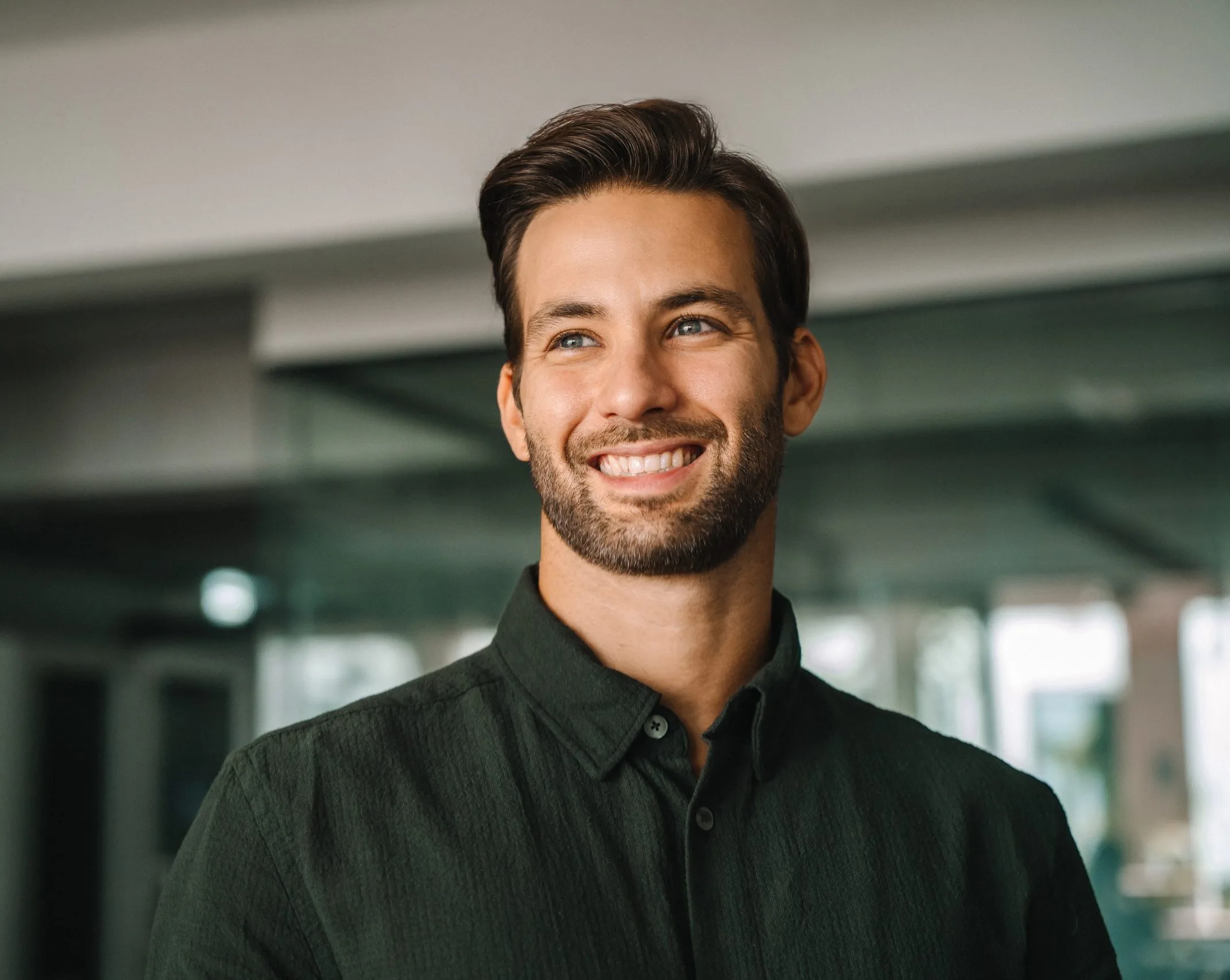 Professional headshot of a smiling man in a dark button-up shirt in a modern office setting