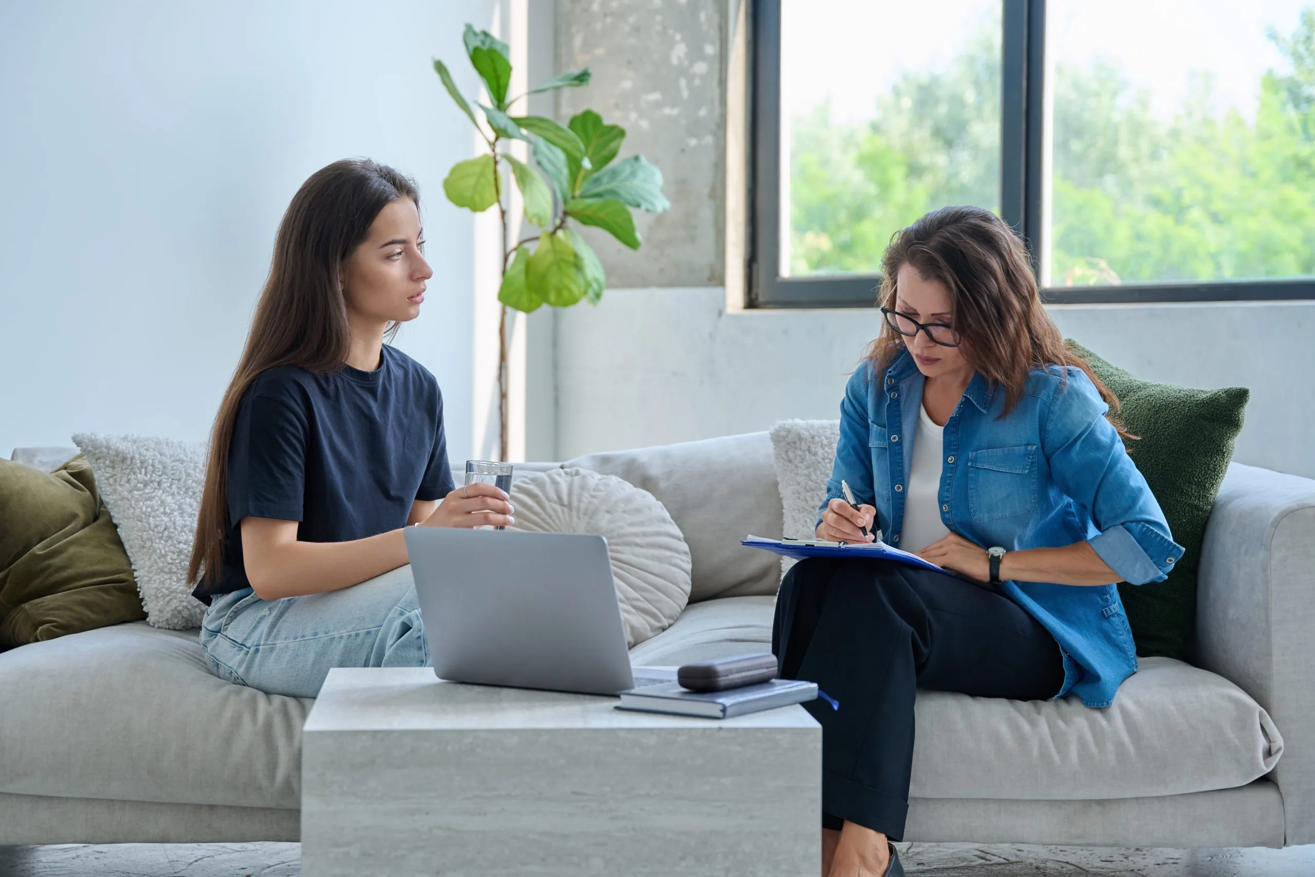 Teenage girl in therapy session with mental health therapist taking notes on couch