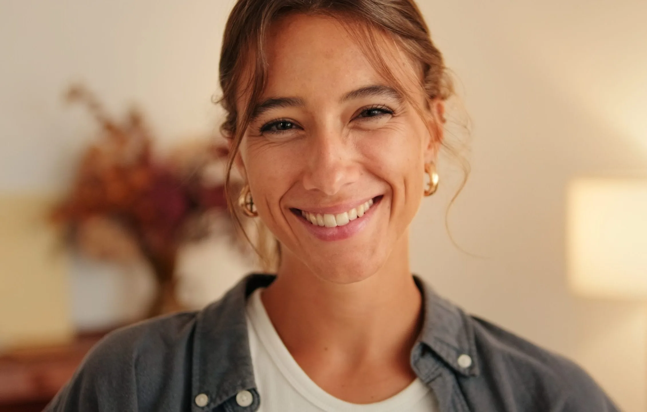 Smiling woman in casual shirt with warm, blurred indoor background