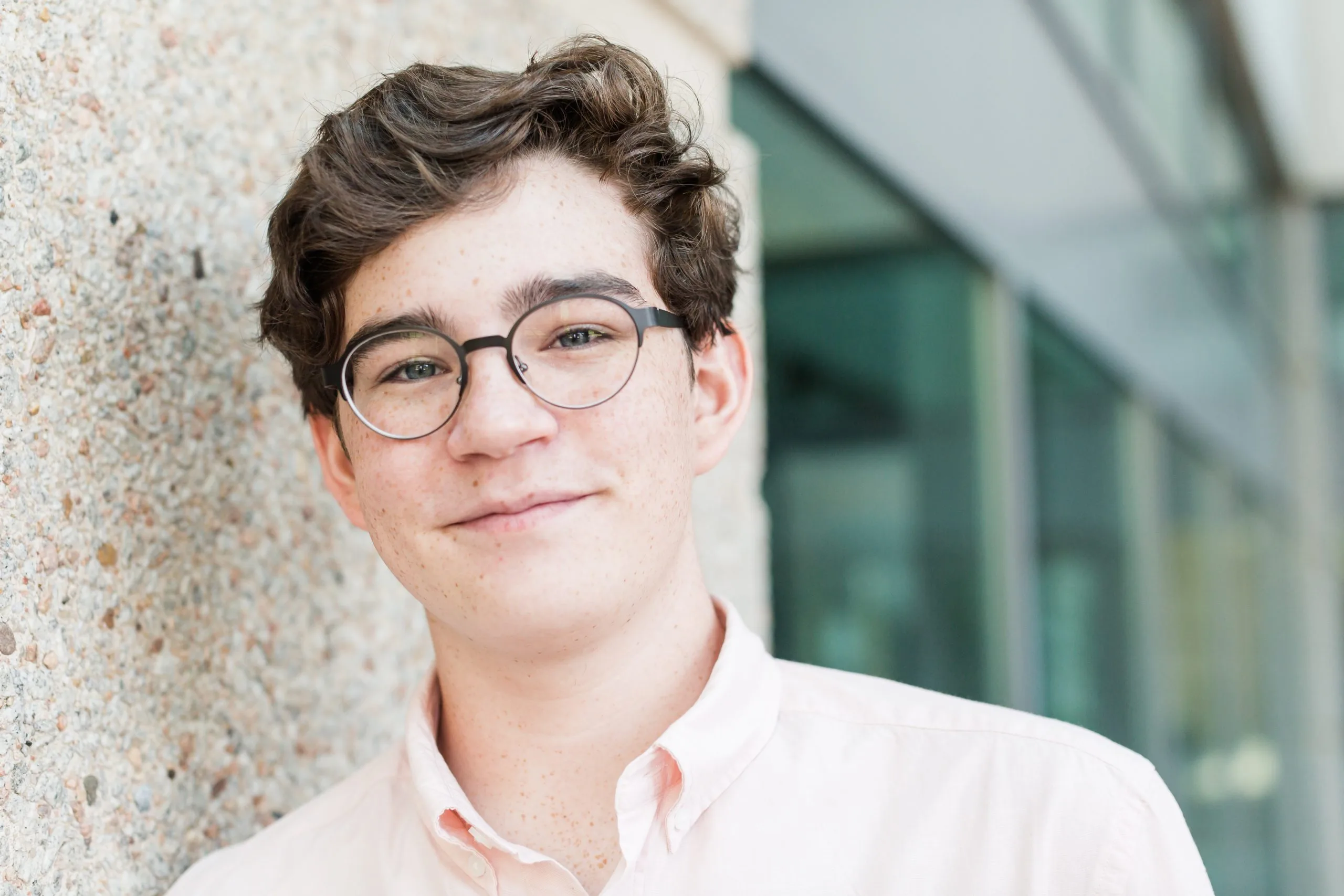 Teenager wearing glasses leaning against a textured wall