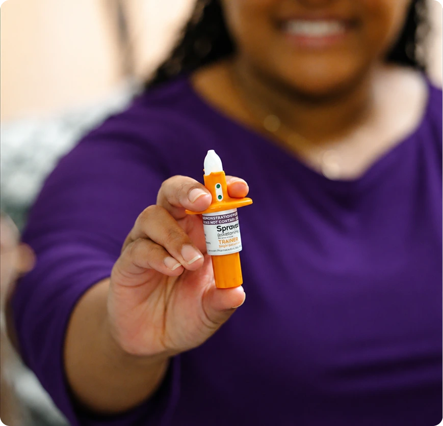Person holding a Spravato nasal spray demonstrator device in an orange and white container