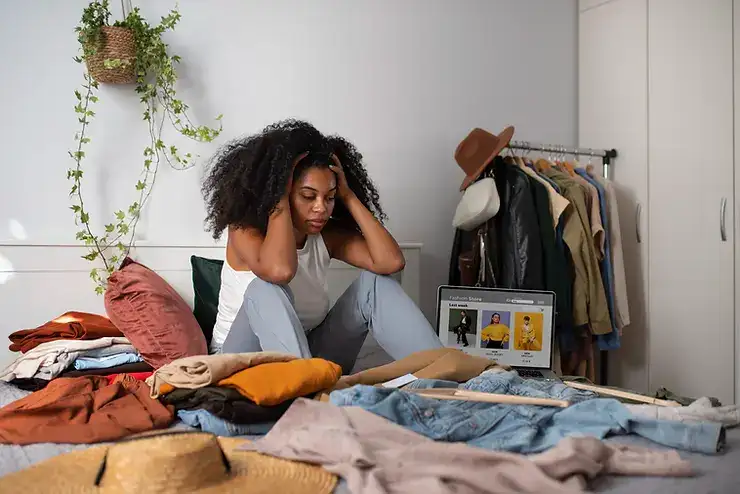 Woman sitting among scattered clothing looking stressed, illustrating anxiety's impact on daily tasks