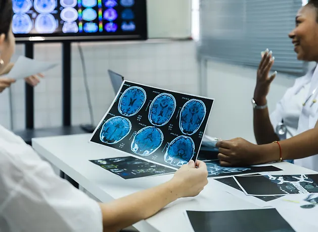 Two clinicians reviewing brain scan images at a desk with additional scans displayed on monitors behind them