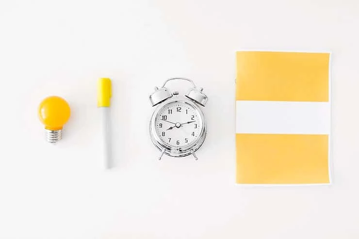 Yellow lightbulb, marker, alarm clock, and sticky notes arranged on white background