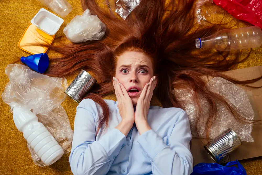 Woman with distressed expression surrounded by scattered trash and recyclables on yellow background