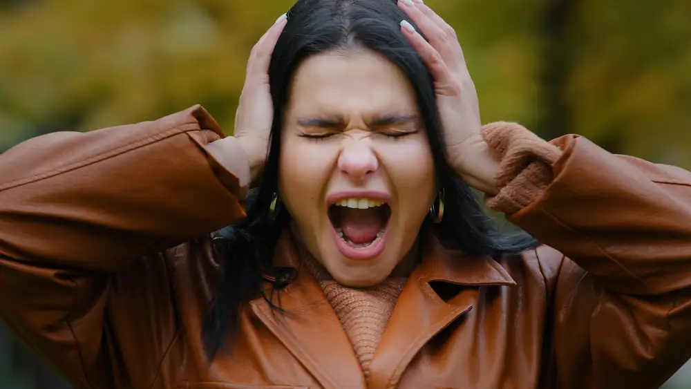 Woman clutching her head with hands on ears, mouth open in distress, showing signs of panic or anxiety