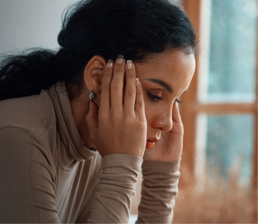 Woman holding her head with both hands, appearing distressed by a window