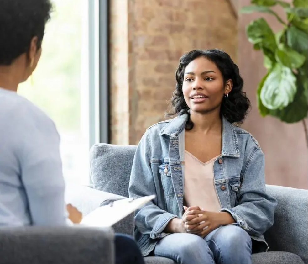 Woman in denim shirt speaking with man during counseling session by window with plant