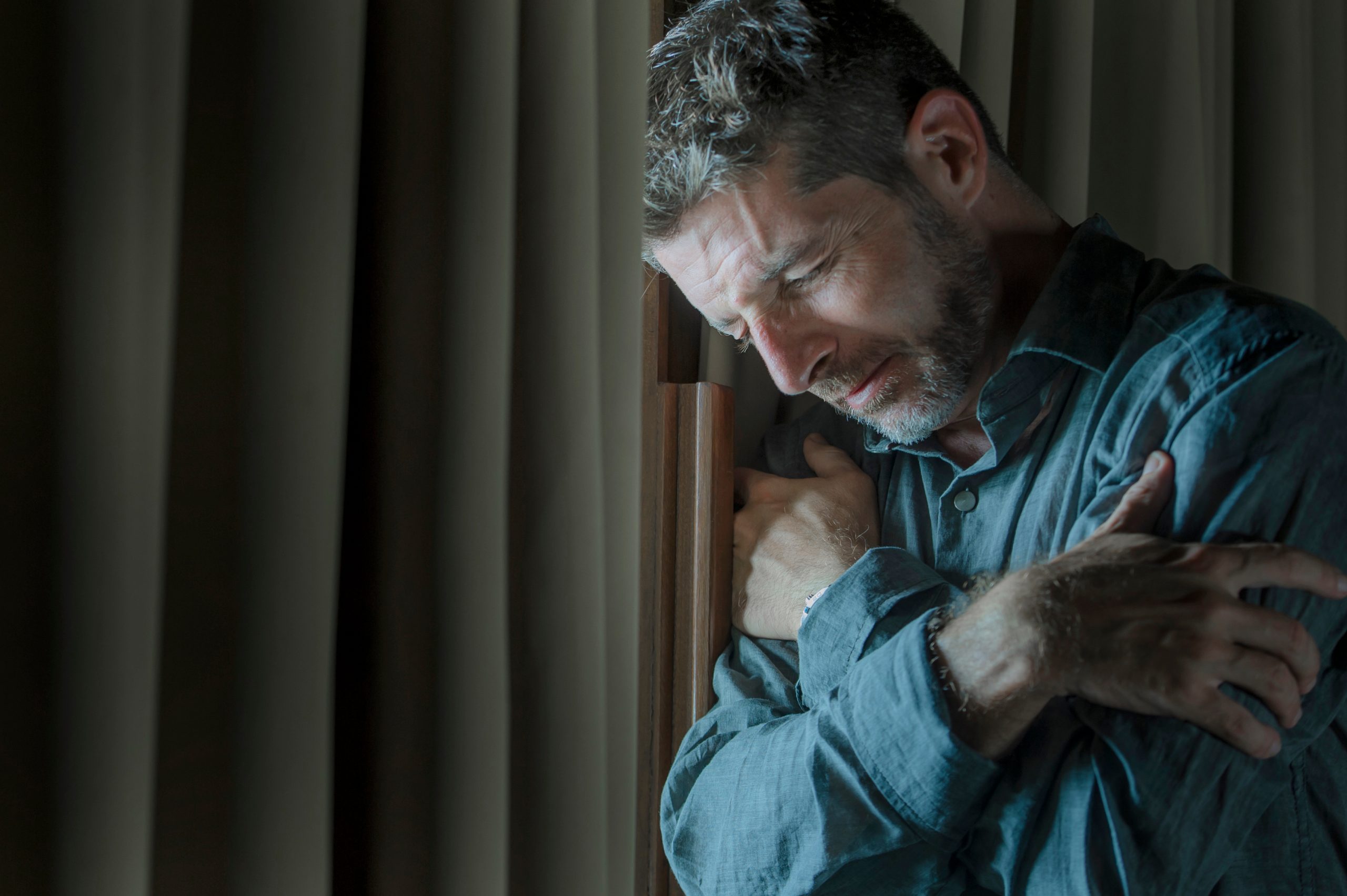 Man holding himself while looking down, expressing emotional distress or sadness indoors