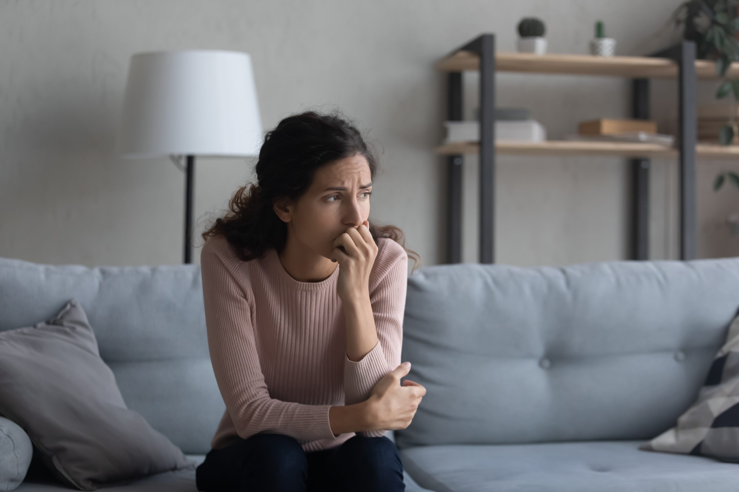 Woman sitting on couch with hand to face, appearing worried or anxious
