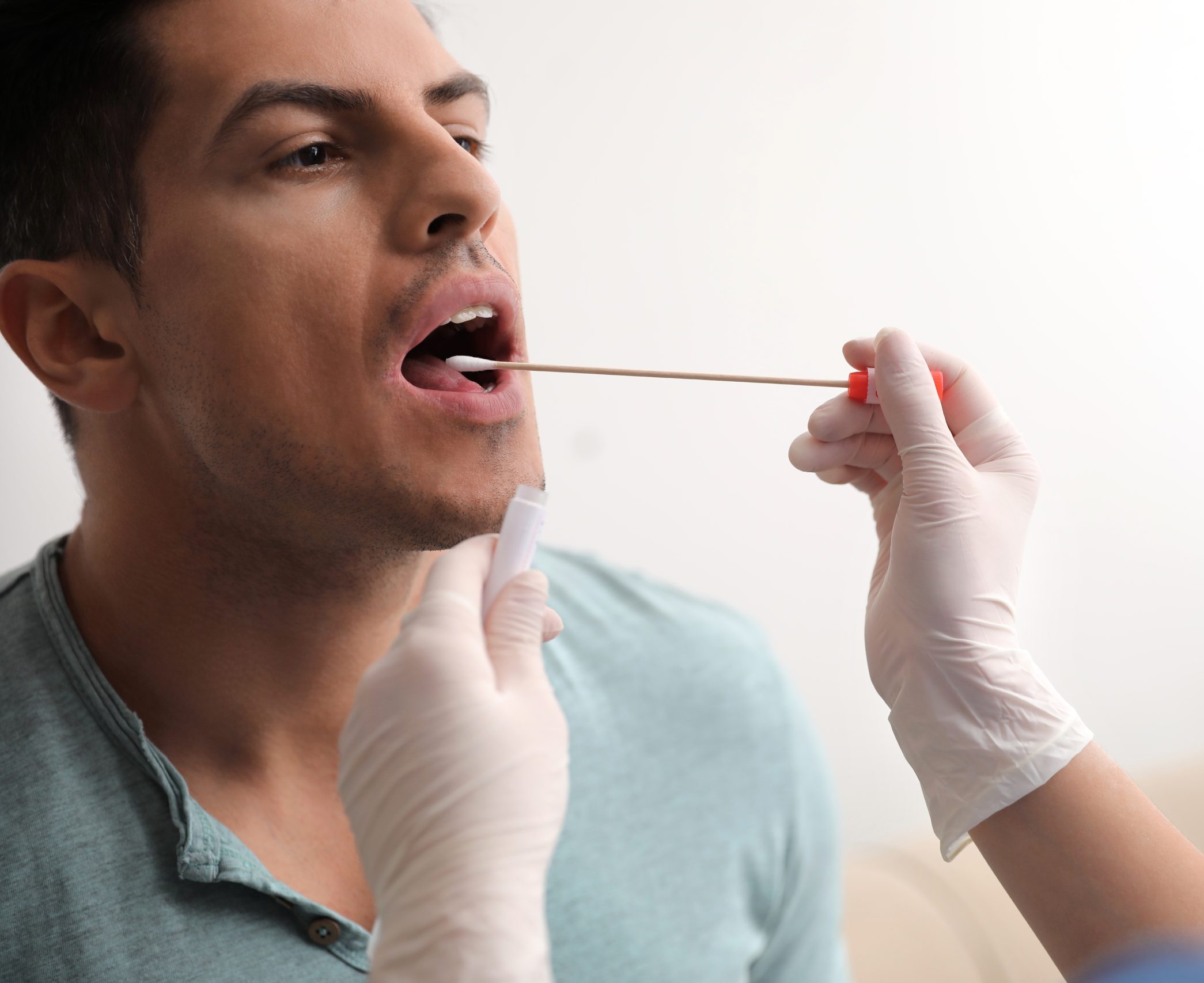 Healthcare provider with gloved hand examining patient's mouth and throat with tongue depressor