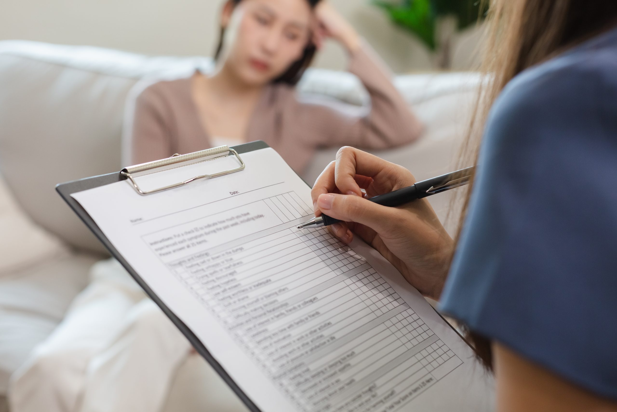 Therapist writing notes on a clipboard while consulting with a patient on a couch