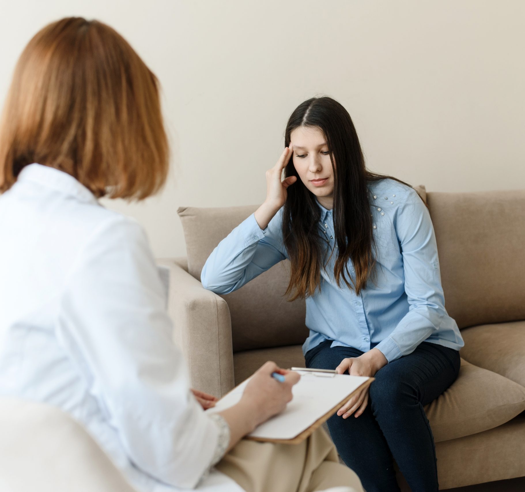 Therapist taking notes while listening to woman on couch during session