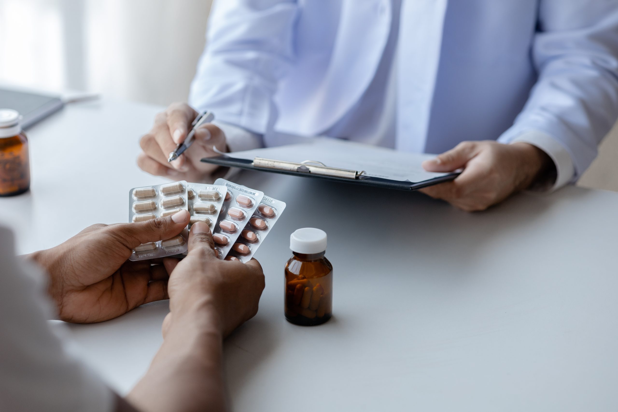 Healthcare provider writing notes while patient displays multiple medication blister packs