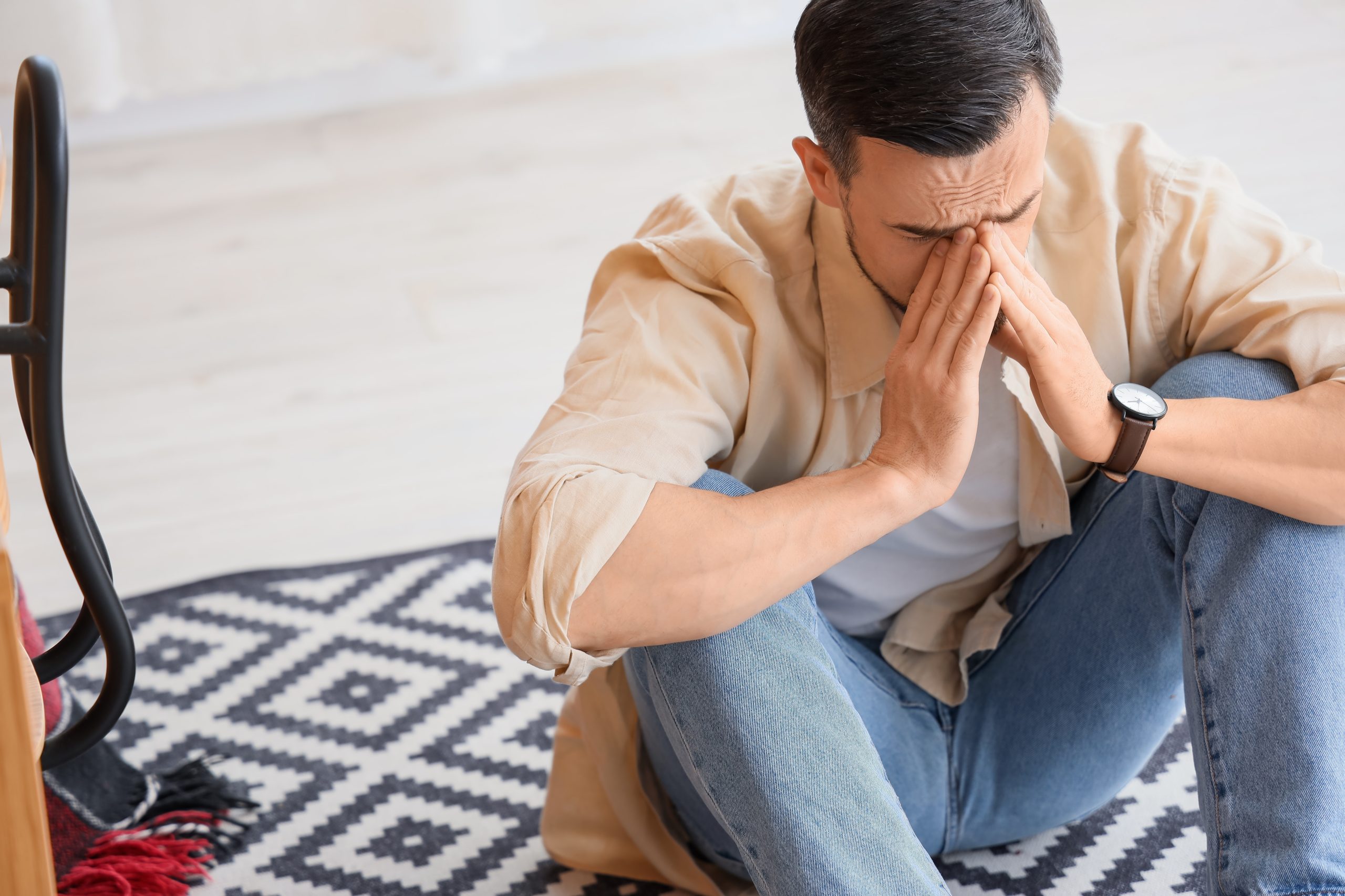 Man sitting on floor with hand to face, looking stressed in front of a monitor