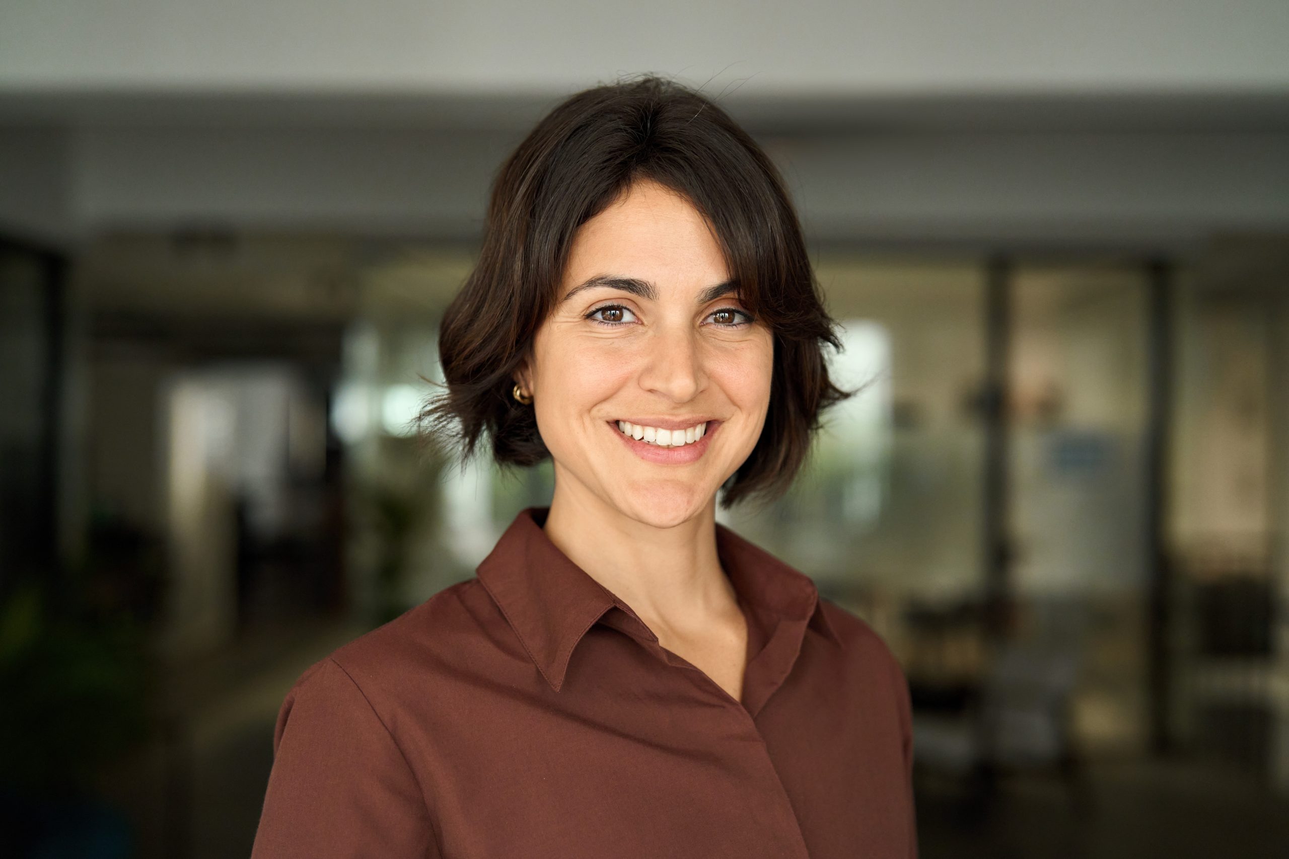Female healthcare professional in burgundy shirt smiling at camera in medical office