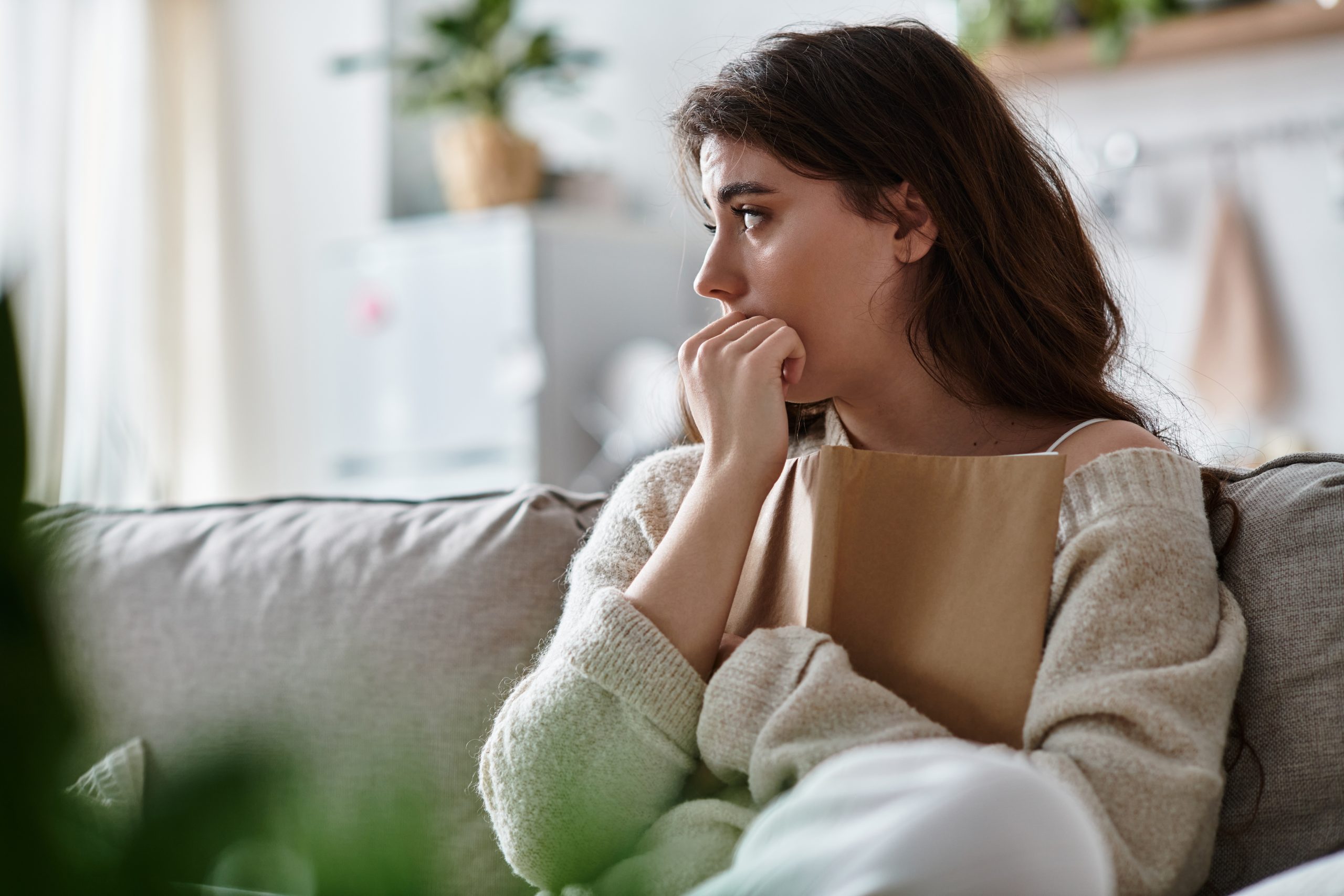 Woman on couch looking worried with hand near mouth