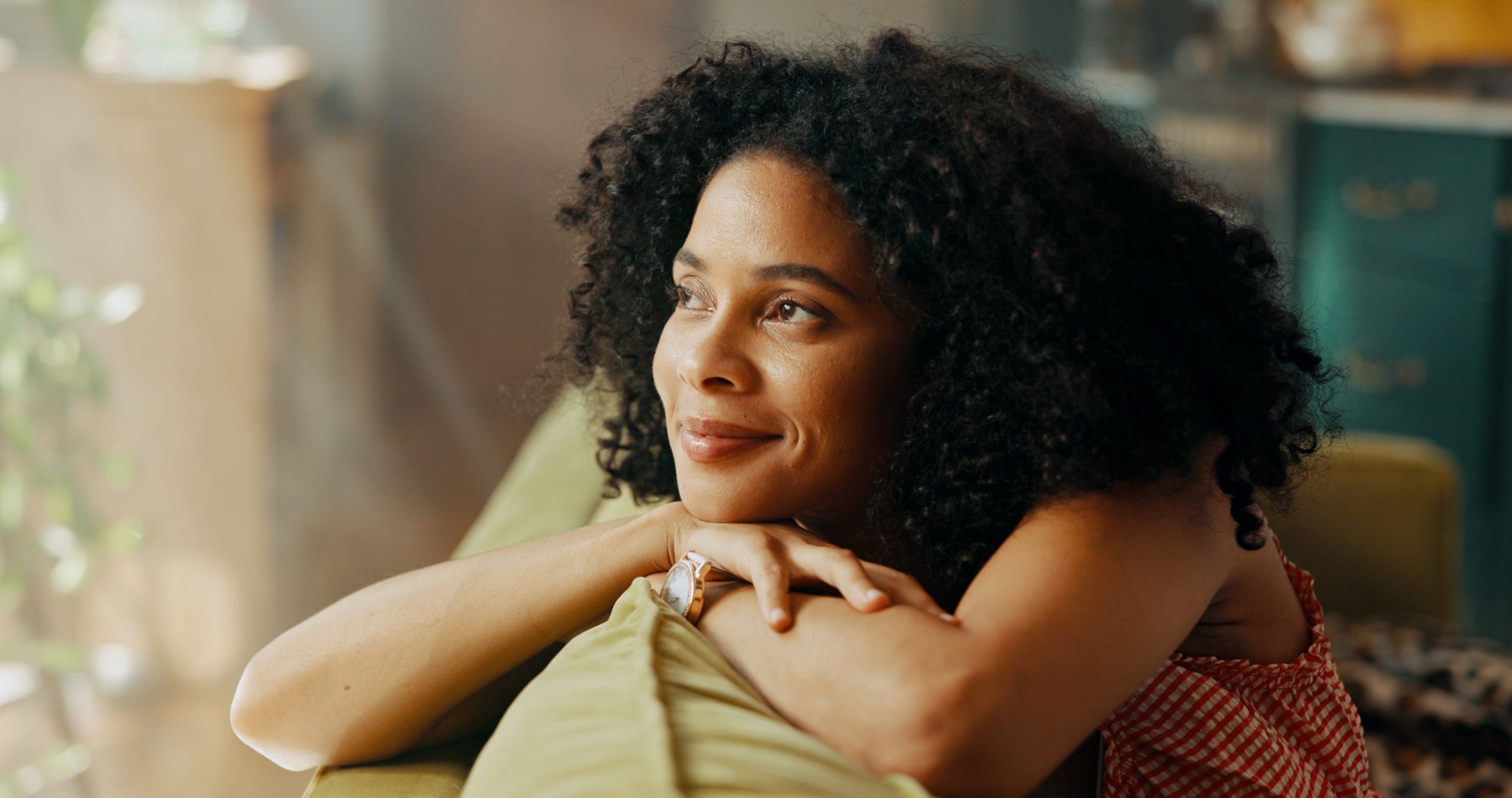 Woman with curly hair smiling while leaning on couch arm