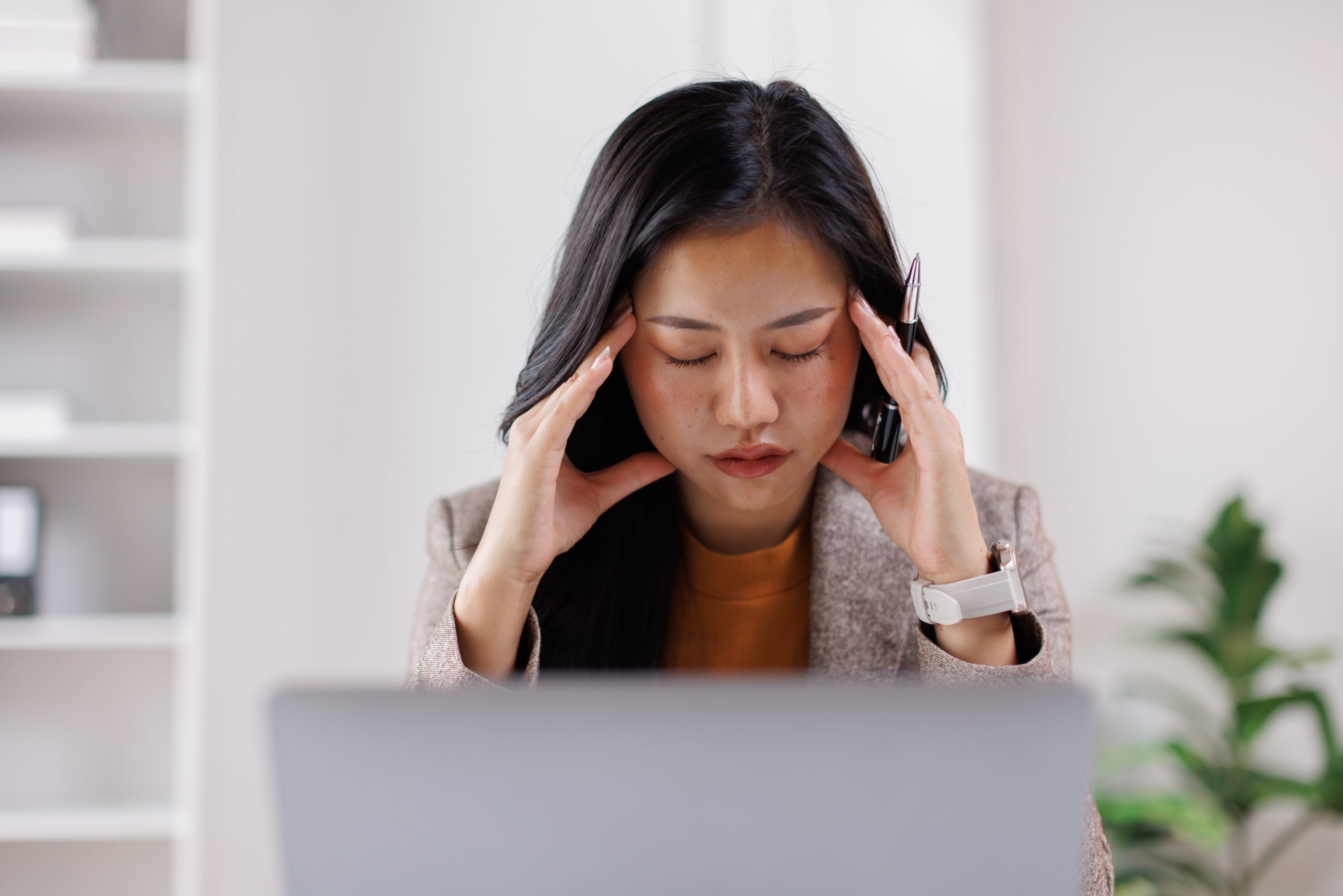 Woman holding her head at laptop, appearing stressed or experiencing headache while working