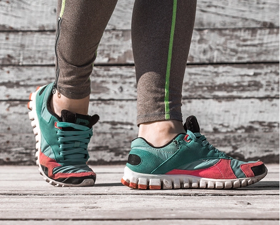 Person wearing teal and red running shoes standing on wooden deck