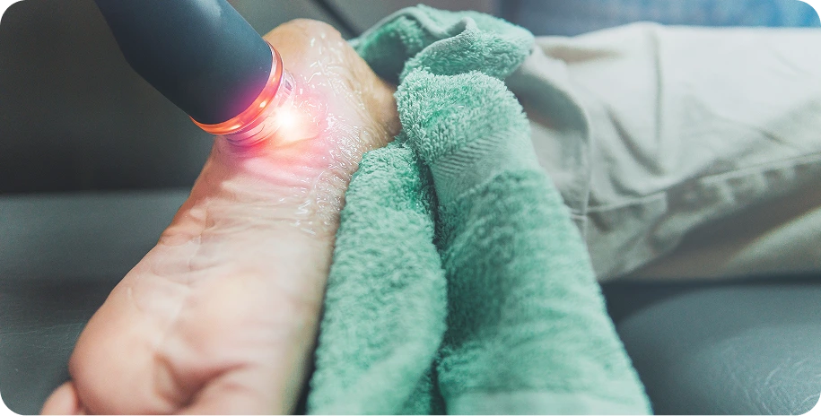High-power laser device applying red therapeutic light to a patient's foot wrapped in green towel
