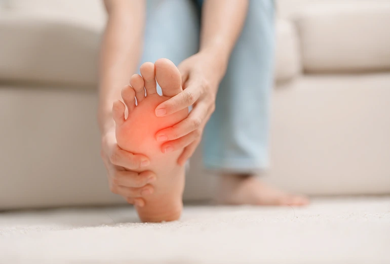Person holding their foot with red highlighted area showing plantar wart pain