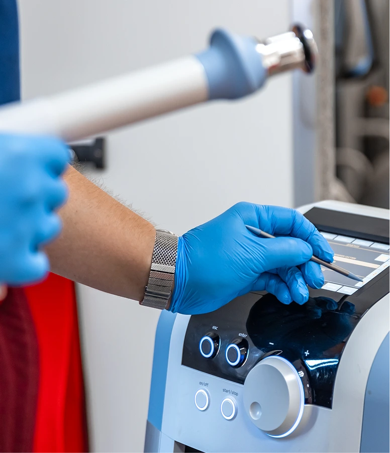 Podiatrist in blue gloves operating laser treatment device on patient's foot