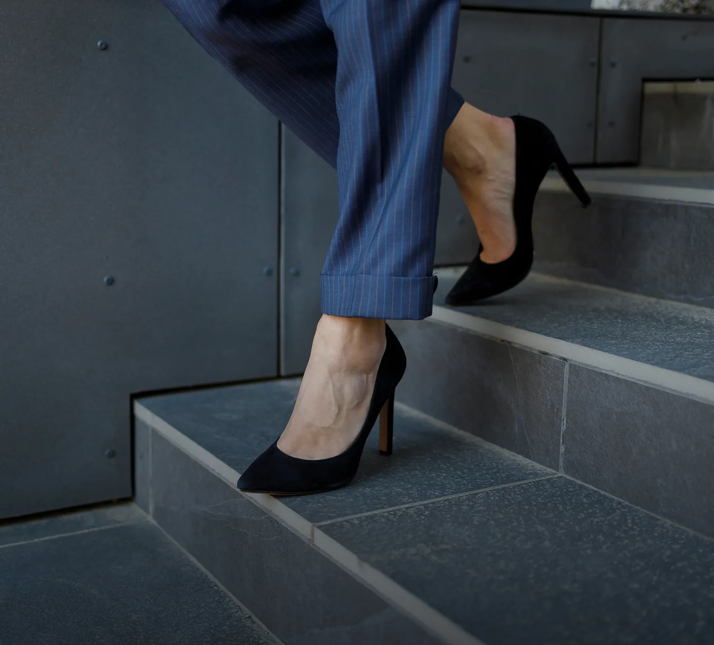 Person climbing stairs wearing black heels and blue pinstriped pants
