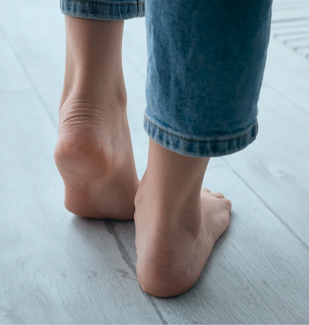 Person's feet and lower legs on light wooden floor wearing denim pants