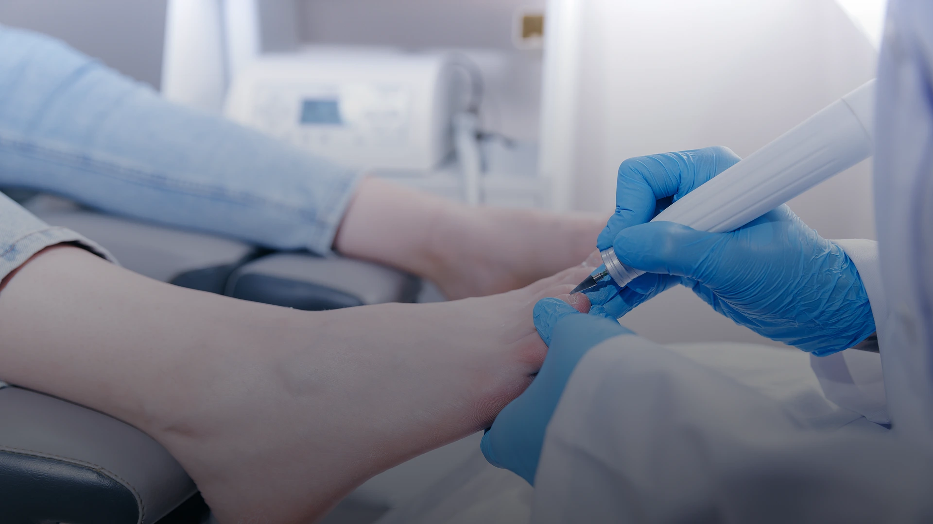 Podiatrist in blue gloves examining a patient's foot with a diagnostic instrument