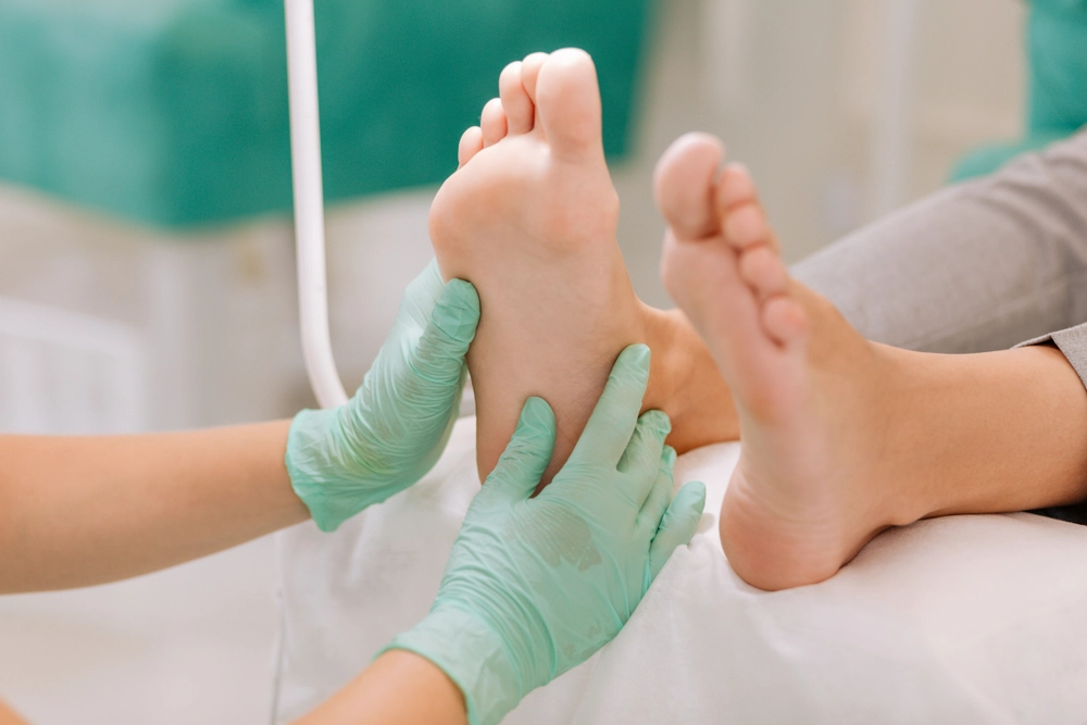 Podiatrist palpating and examining patient's foot and ankle with gloved hands