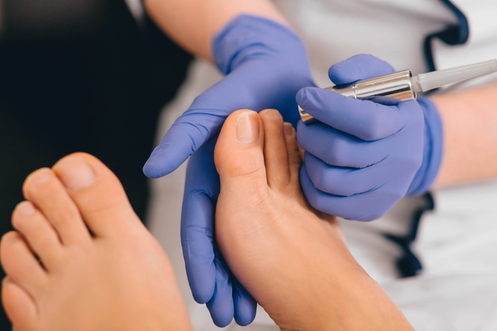 Podiatrist in blue gloves using handheld device to examine patient's toenails
