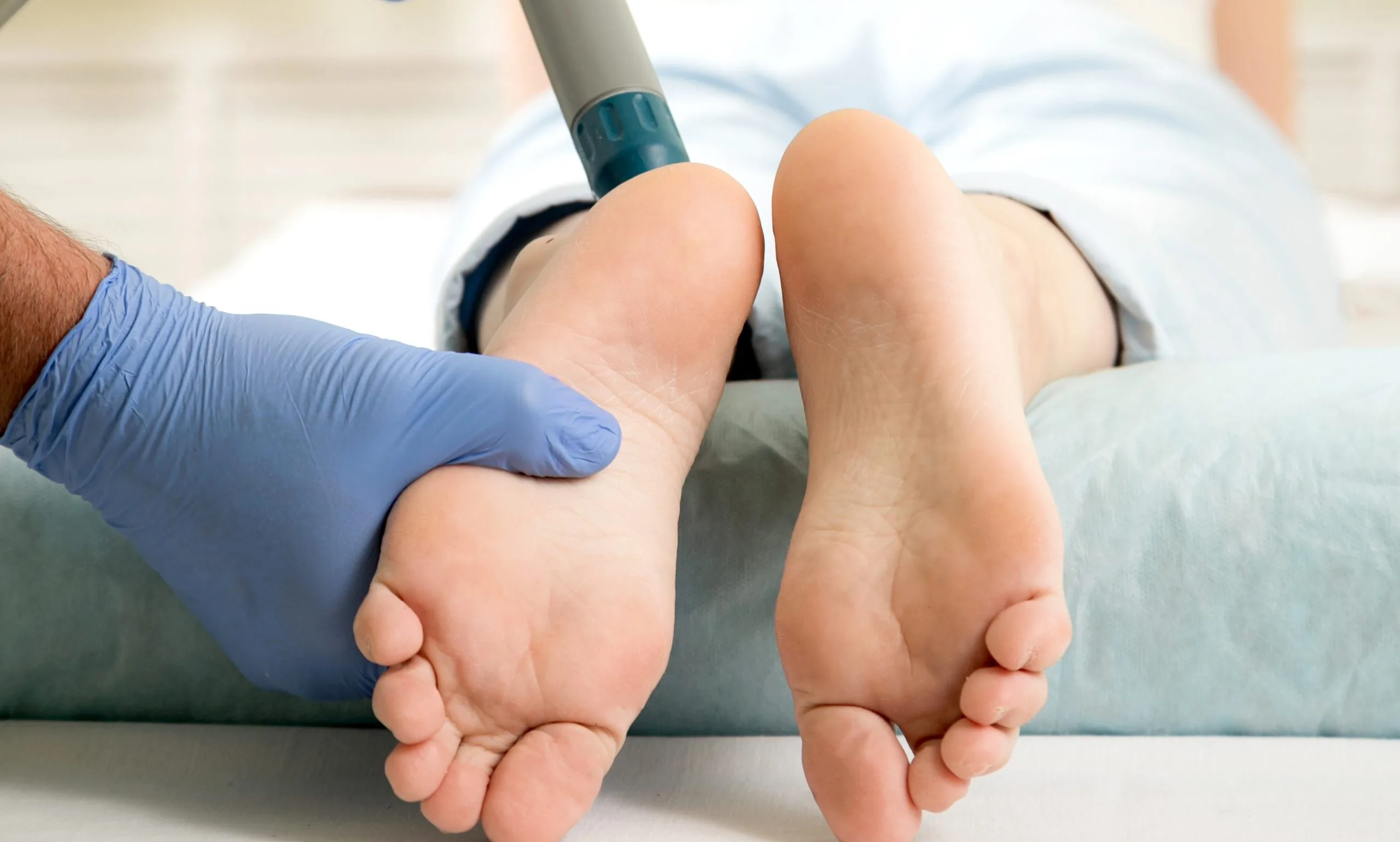 Podiatrist in blue gloves examining patient's foot with handheld device