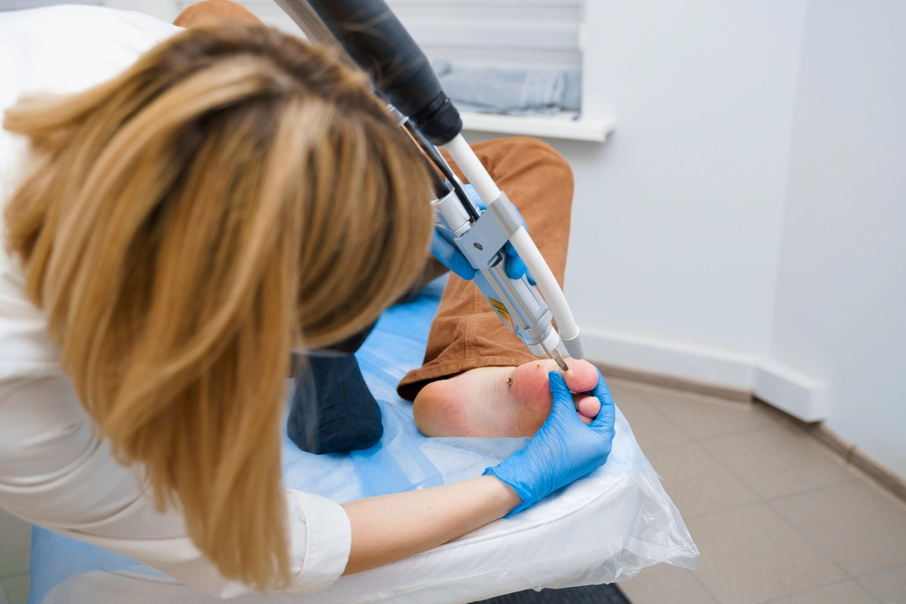 Clinician using laser device to treat patient's heel during podiatric procedure