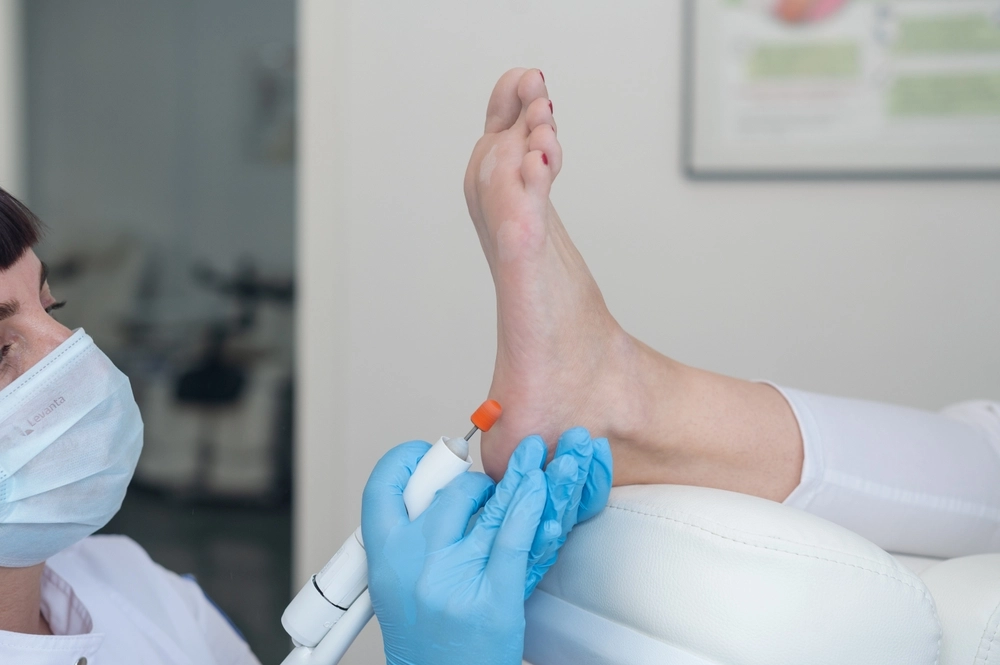 Podiatrist applying laser treatment device to patient's heel in clinical setting