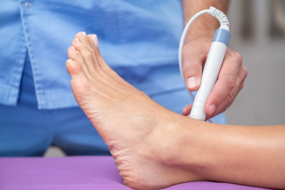 Podiatrist in blue uniform examining patient's foot with handheld diagnostic device
