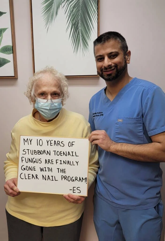 Patient holding sign reading 'My 10 years of stubborn toenail fungus are finally gone with the clear nail program!' with podiatrist in blue scrubs