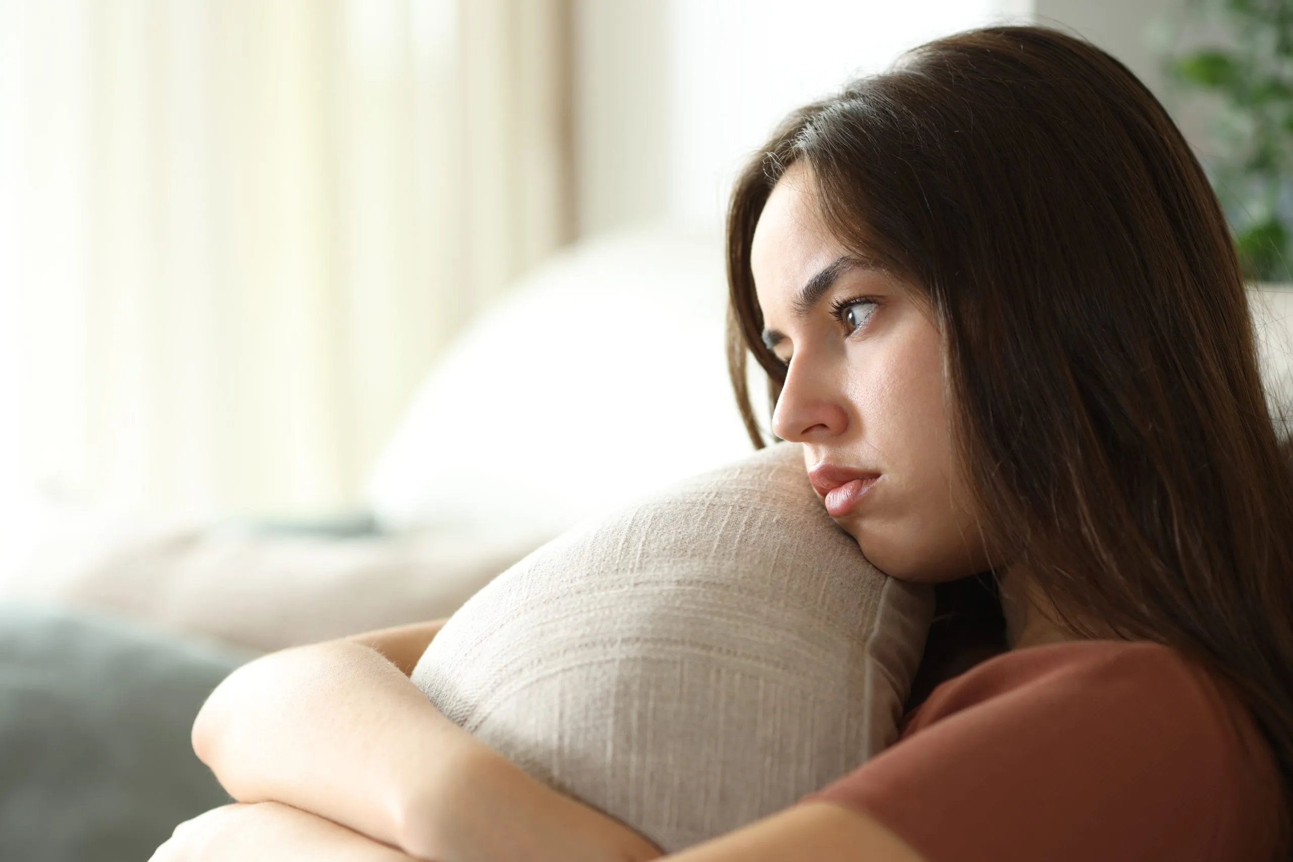 Sad woman hugging a pillow on a sofa before starting psychiatric care