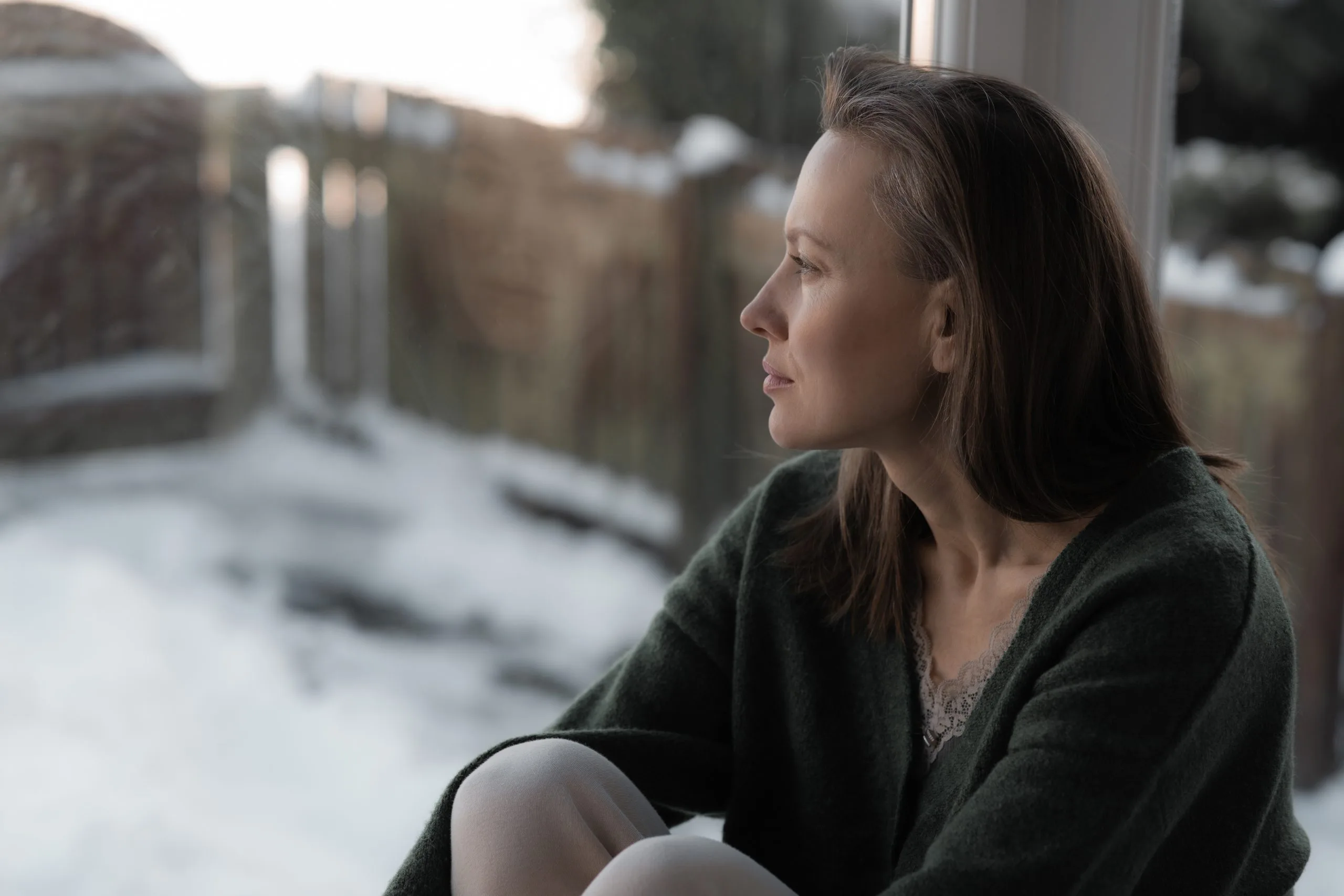 Thoughtful woman sitting on a windowsill reflecting on her mental health