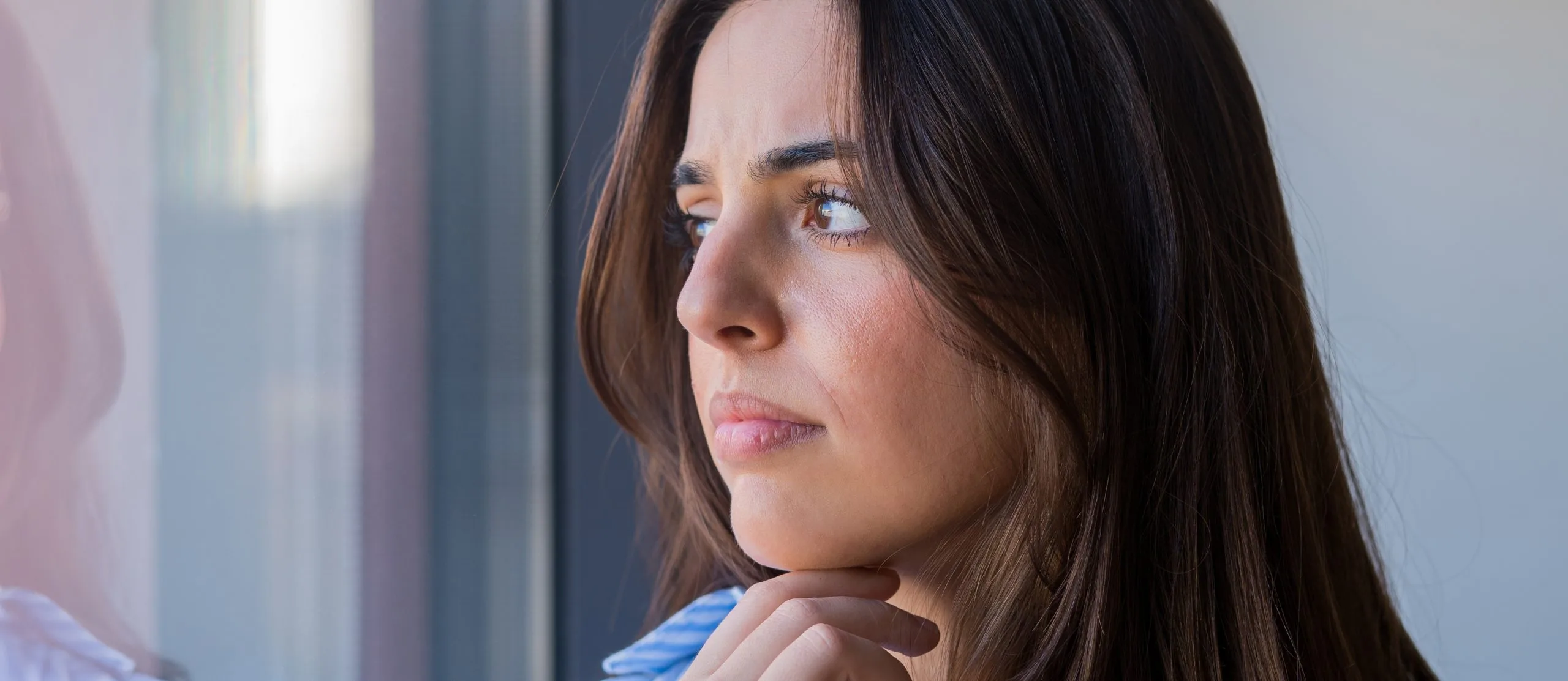 Worried young woman looking out a window feeling anxious