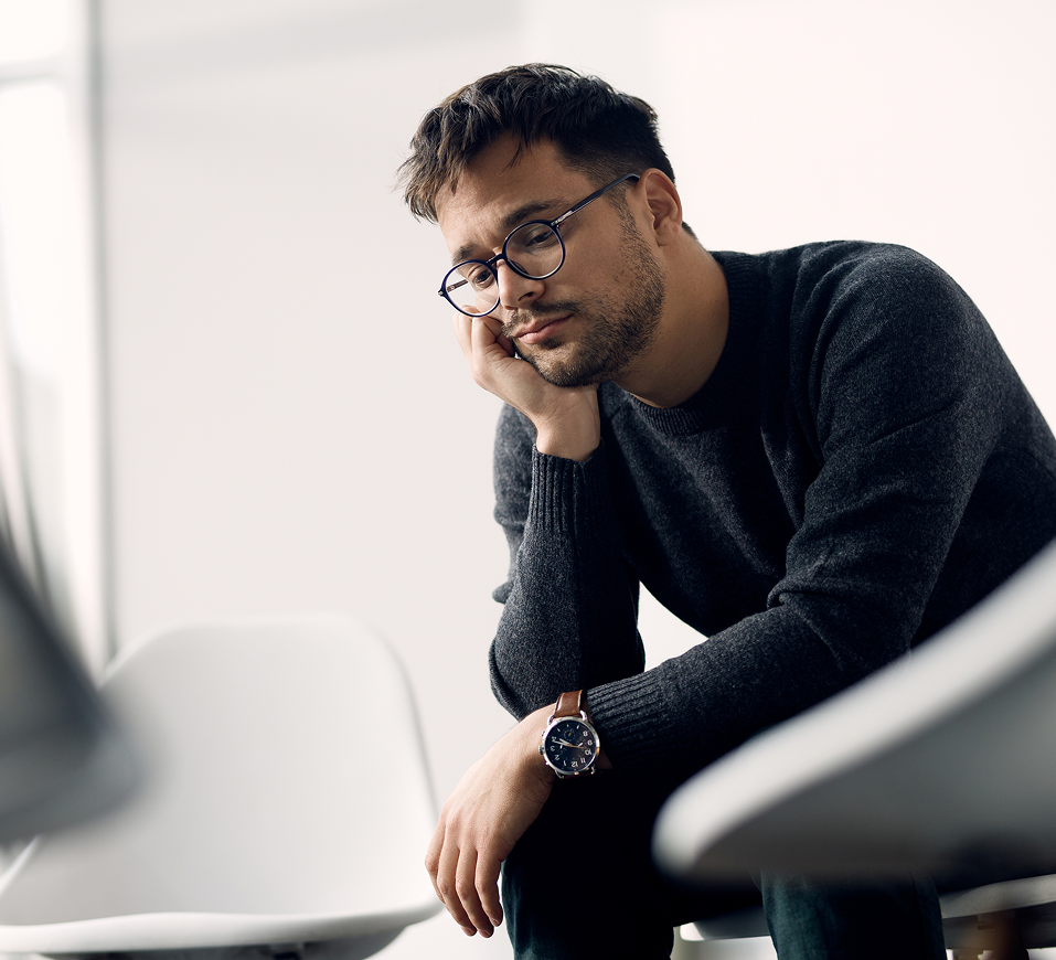 Man wearing glasses with hand to face in contemplative pose indoors