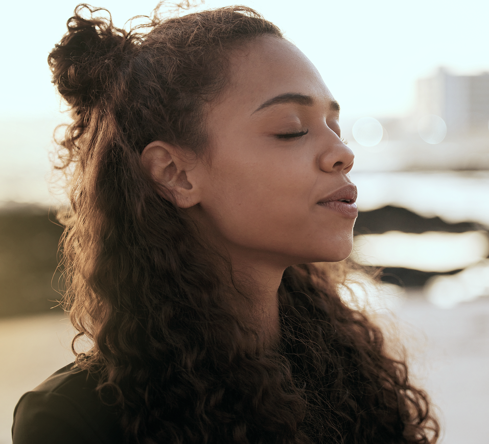 Woman with eyes closed and peaceful expression outdoors by water