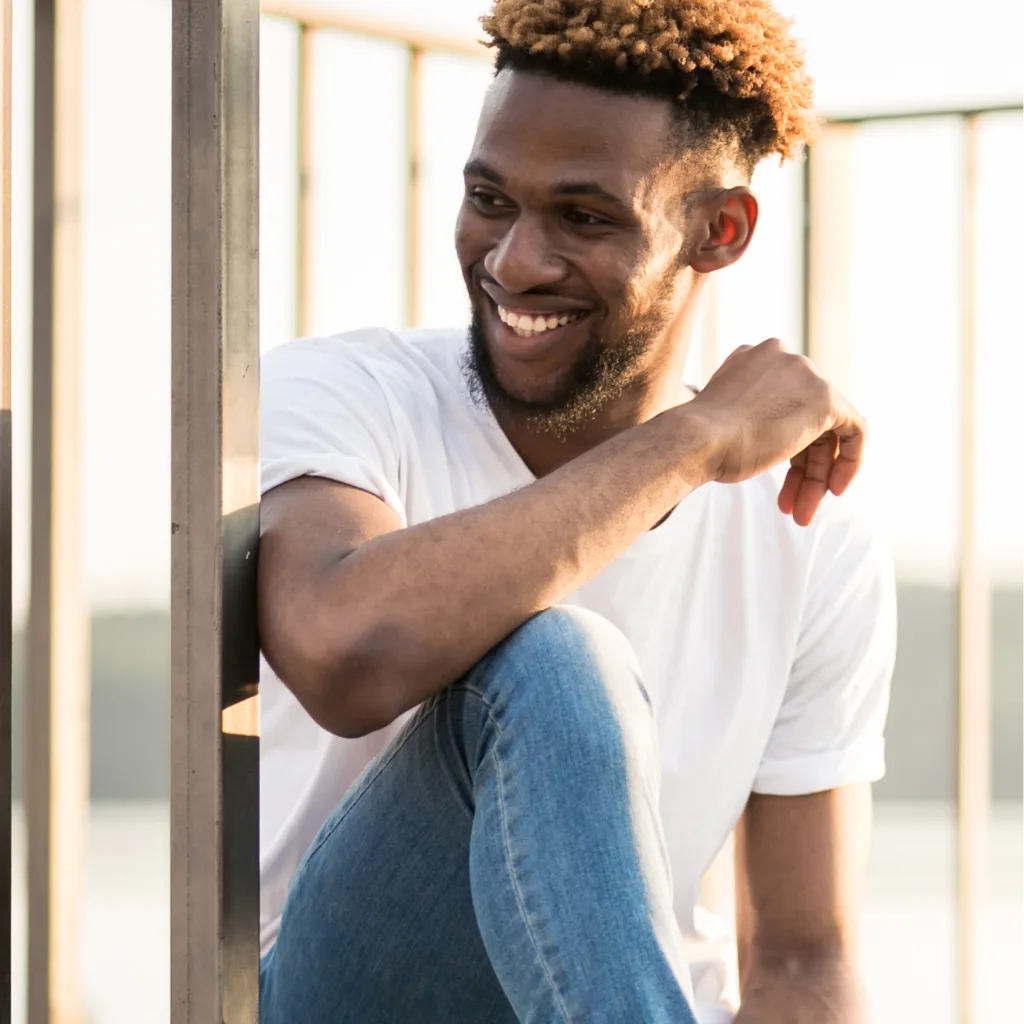 Man in white shirt and jeans smiling by a bright window