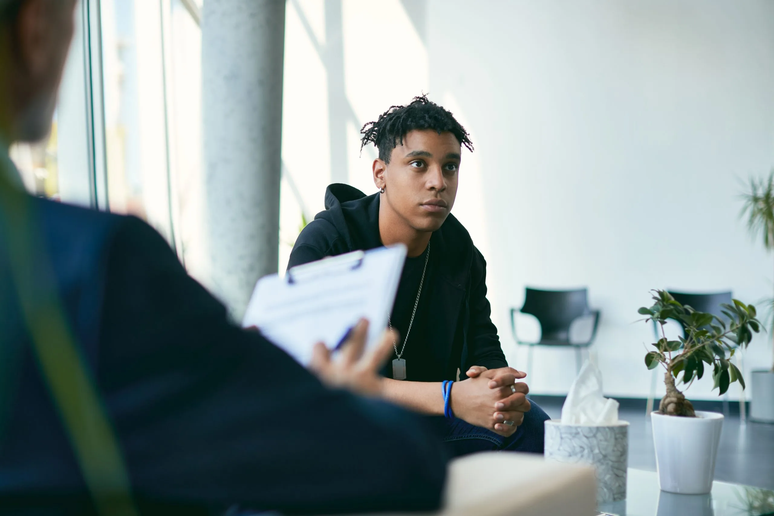 Adolescent patient in session with psychiatrist holding clipboard during appointment