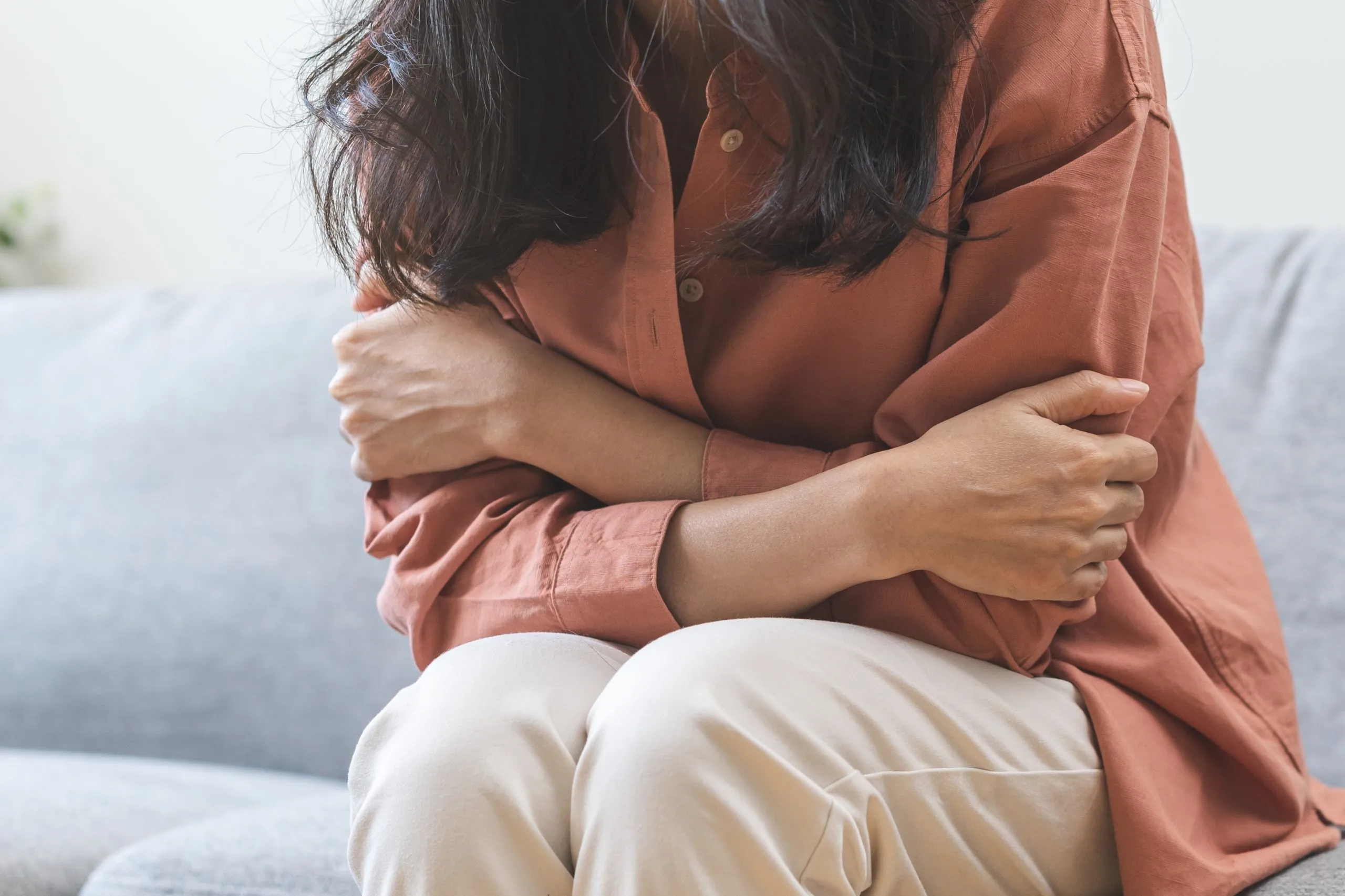 Woman in rust-colored shirt hugging herself while sitting on couch